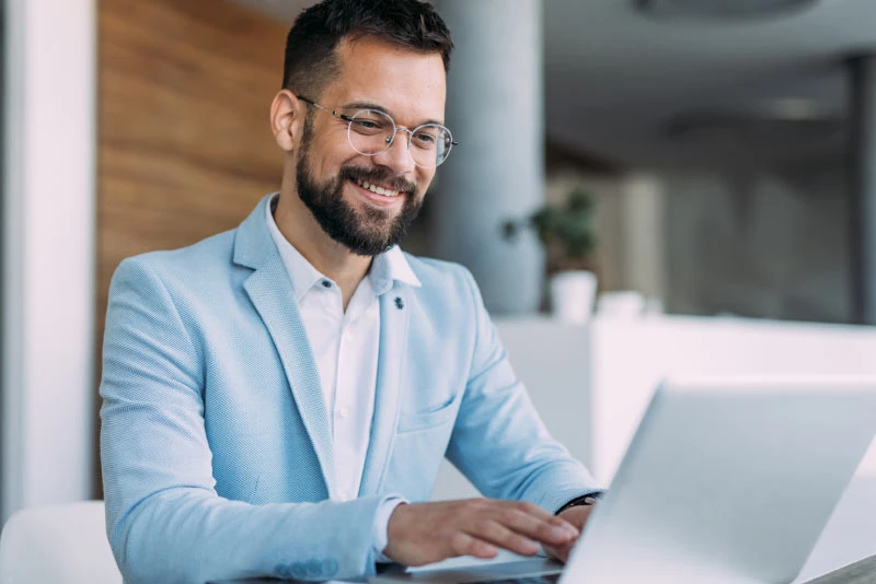 A photo of a young businessman smiling while using his laptop in an office